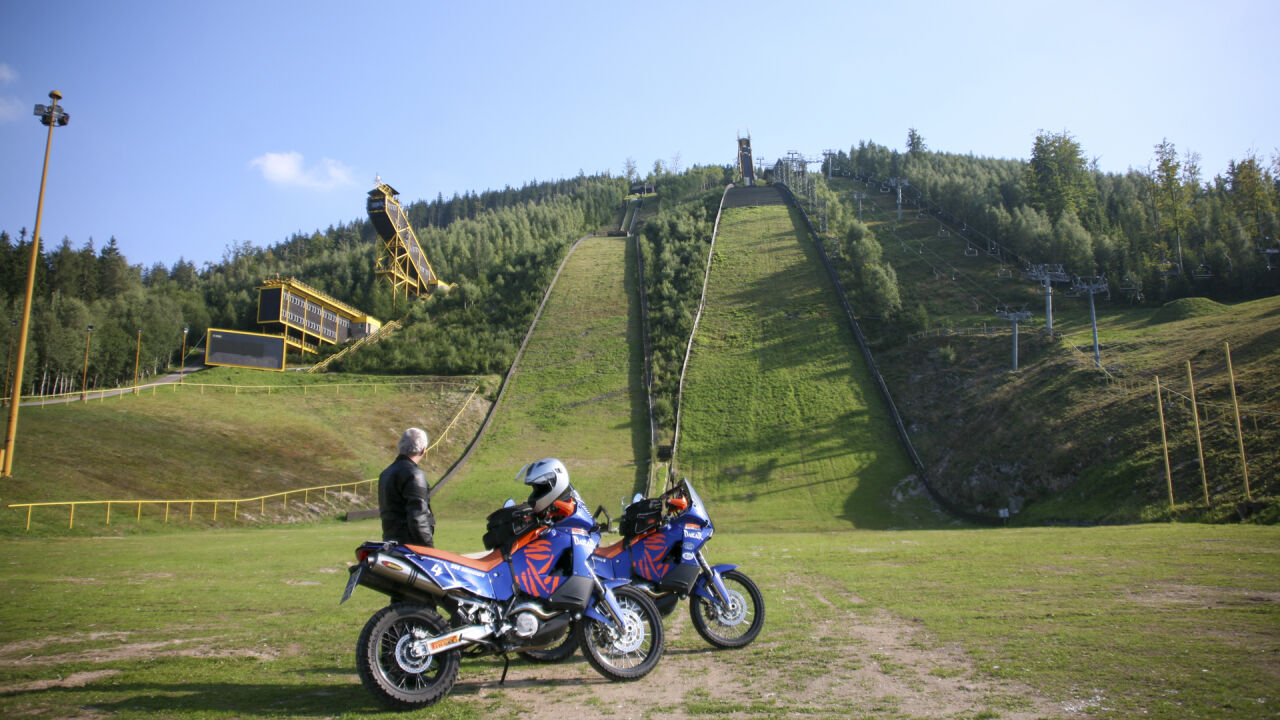 Zwei Reiseenduros vor einer großen Skisprungschanze am Waldhang