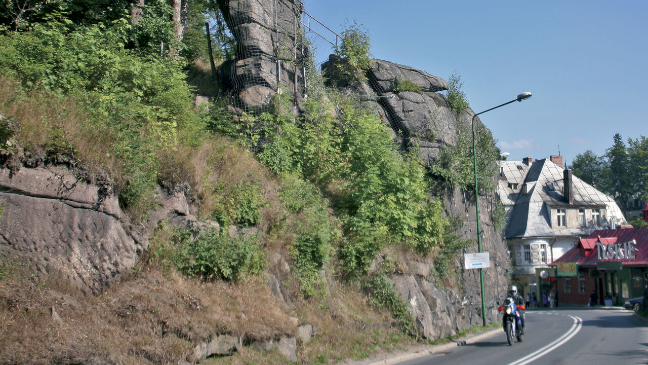 Motorrad auf einer Ortsstraße unter einer Felswand, daneben ein Haus mit Leuchtreklame
